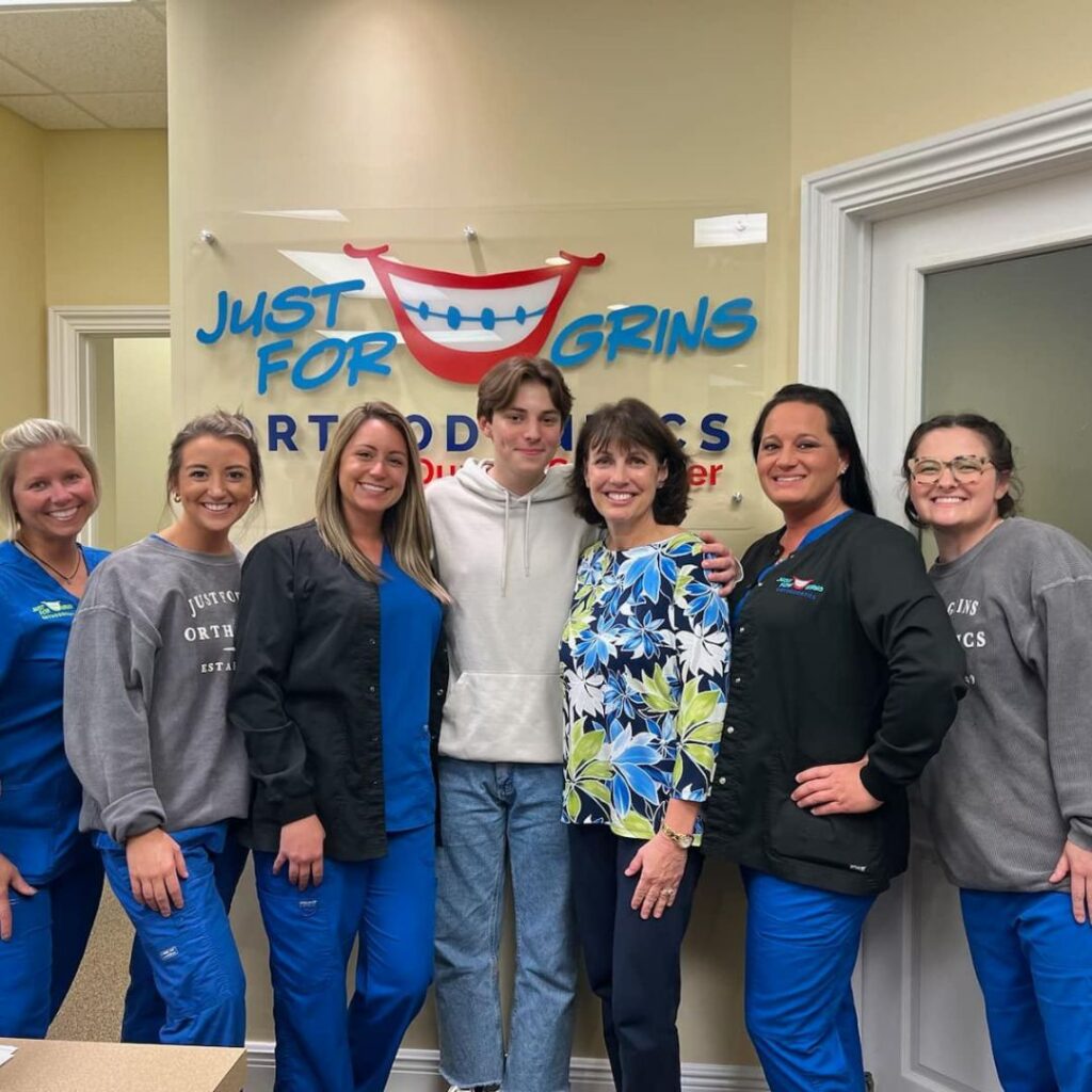 Dr Dunn and team members and patients smiling in front of JFG logo in lobby